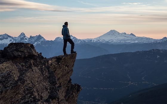 Hiker on rocky outcropping, looking over mountain range