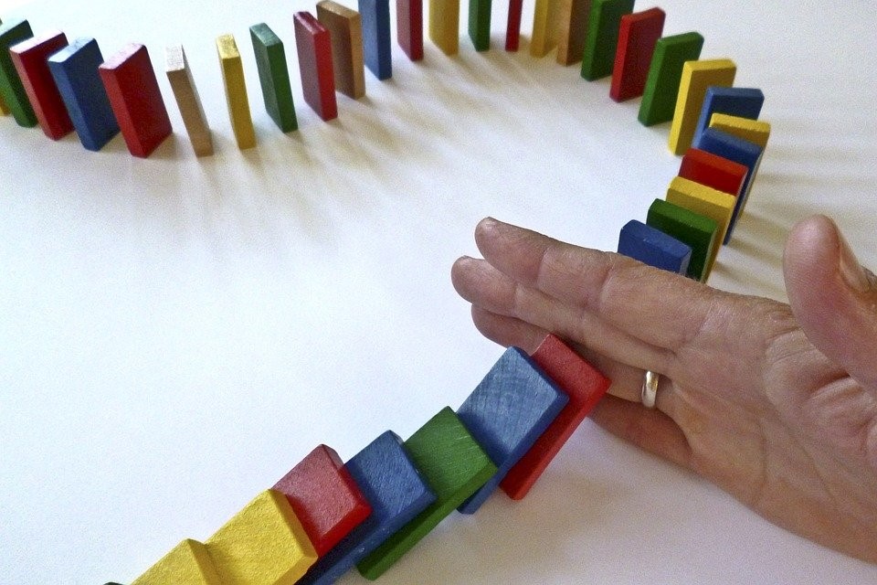 A person's hand stopping dominoes from falling.